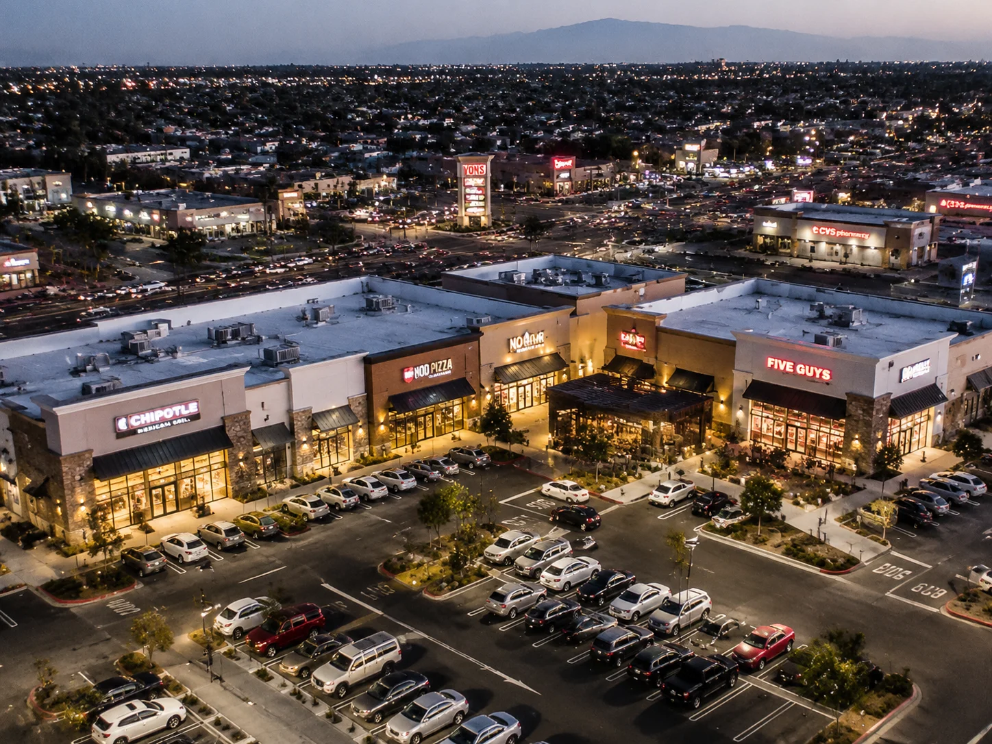 Aerial-Aufnahme einer amerikanischen Suburban-Shopping-Plaza mit mehreren Restaurant-Fassaden bei Abendbeleuchtung, urbane Dichte, dokumentarischer Stil
