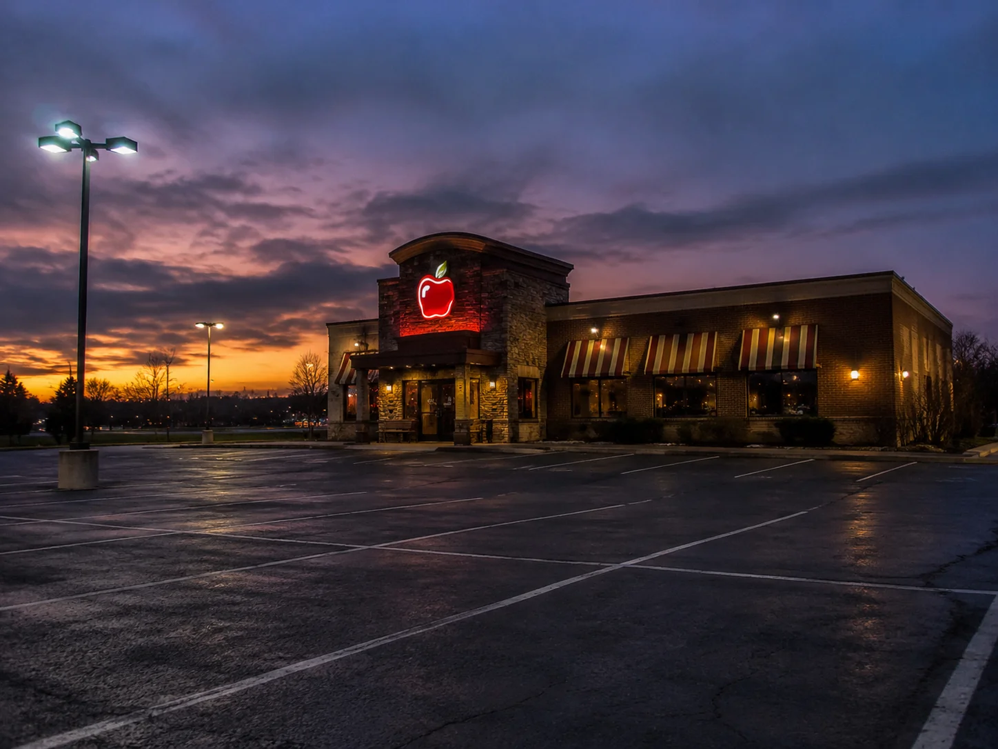 Cinematic-Aufnahme eines leeren Parkplatzes vor einem amerikanischen Casual-Dining-Kettenrestaurant bei Abenddämmerung, melancholische Atmosphäre