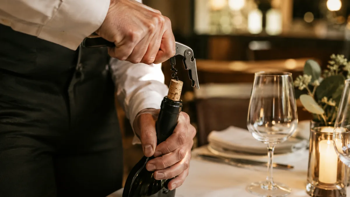 Servicekraft öffnet am Tisch eine mitgebrachte Weinflasche mit dem Kellnermesser