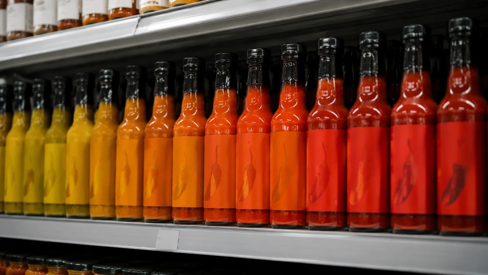 Reihe Chili-Sauce-Flaschen auf einem Supermarktregal mit Spice-Level-Farbcodierung von Gelb bis Tiefrot