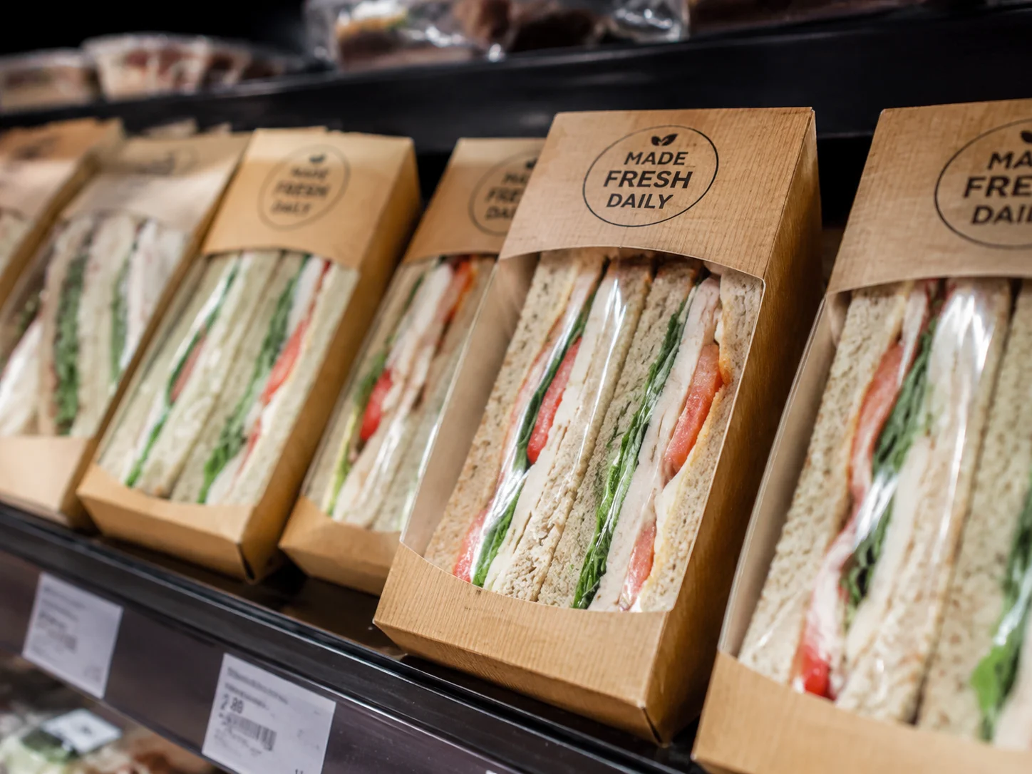 Close-up von vorgefertigten frischen Sandwiches in Karton-Verpackungen auf einem Kühlregal mit Grab-and-Go-Ästhetik, neutrale Beleuchtung