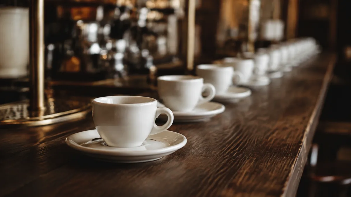 Eine Espressotasse scharf im Vordergrund, dahinter eine lange Reihe identischer Tassen