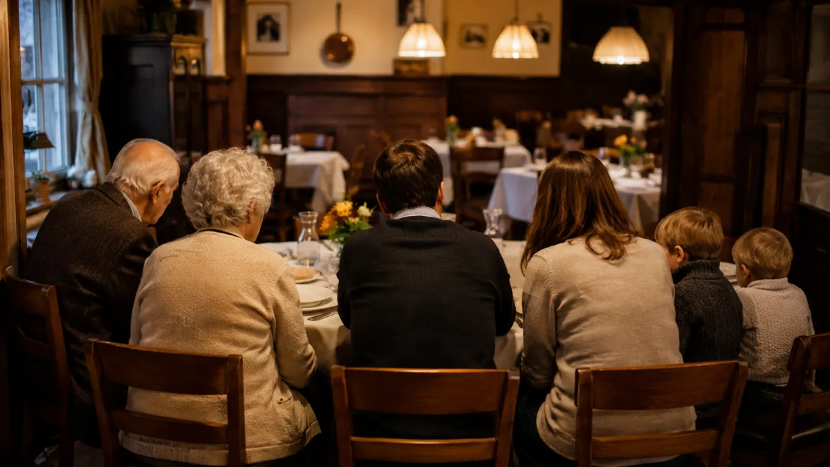 Drei Generationen einer Familie von hinten an einem runden gedeckten Restauranttisch mit weisser Tischdecke und kleiner Blumenvase in einem warm beleuchteten deutschen Gasthaus