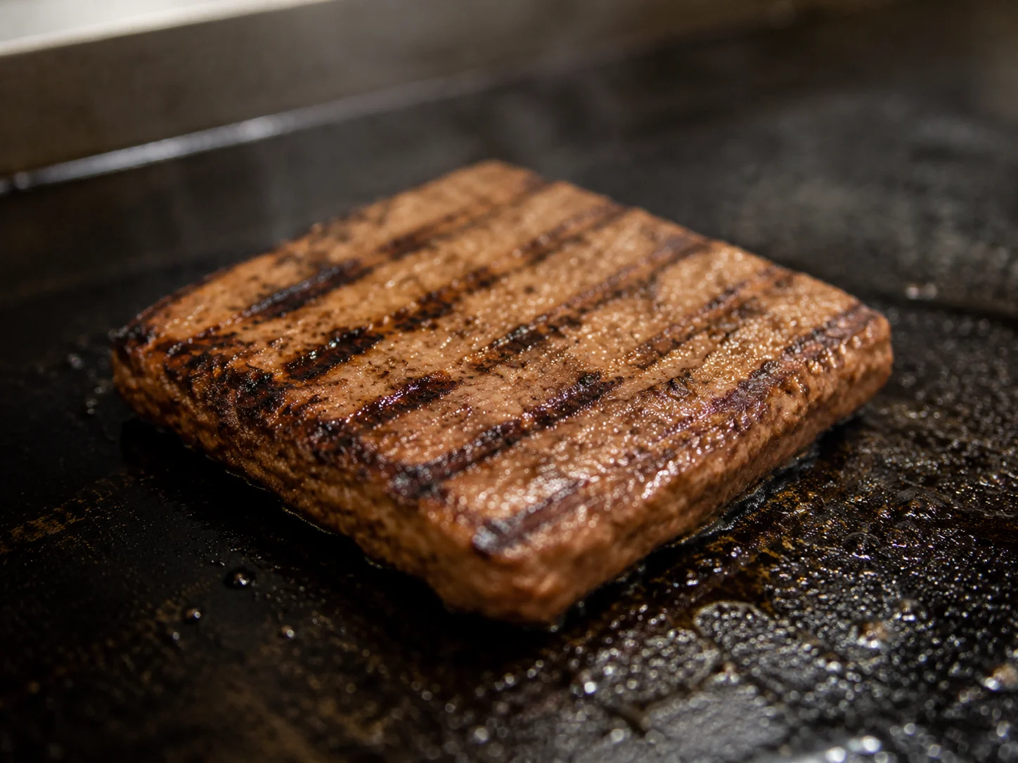 Makro-Aufnahme einer quadratischen Burger-Patty auf Flat-Top-Grill mit Grillmarken, professionelle Küchenbeleuchtung, geometrischer Form-Faktor